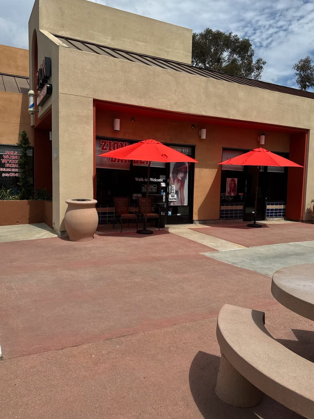 Front entrance of Zion Salon & Barber Shop with outdoor seating and red umbrellas in National City, California.