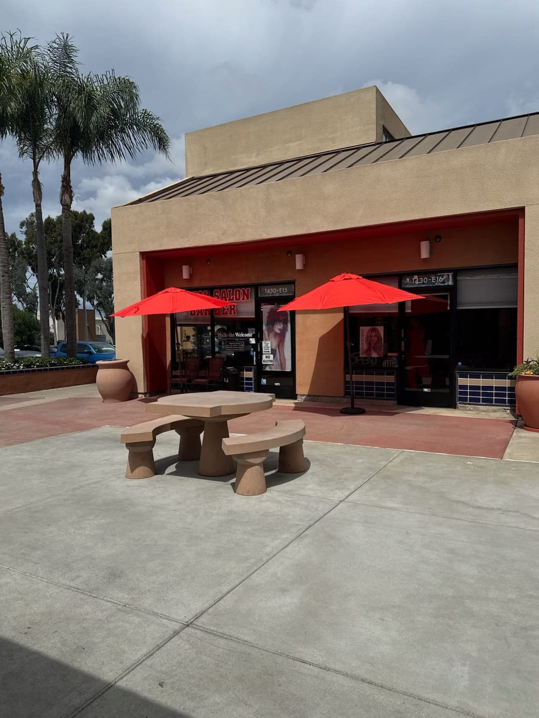 Wide exterior view of Zion Salon & Barber Shop plaza location with red umbrellas and courtyard seating in National City.