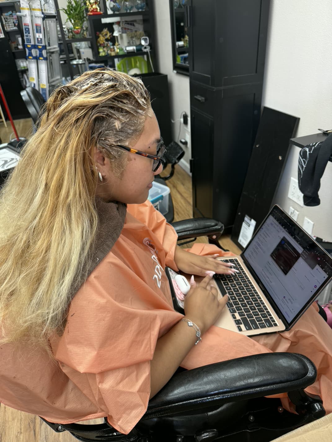 Client with long highlighted blonde hair using a laptop during a salon appointment at Zion Salon & Barber Shop in National City.